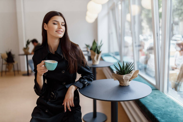 όμορφο κορίτσι σε μια καφετέρια με ένα φλιτζάνι καφέ. - Φωτογραφία, εικόνα