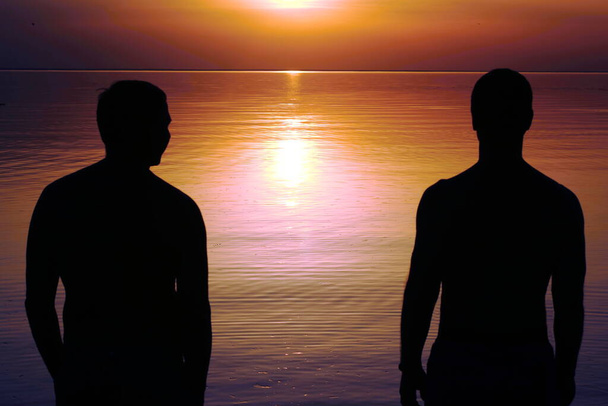 Deux silhouettes d'hommes au coucher du soleil. Une promenade romantique au bord de la mer. - Photo, image