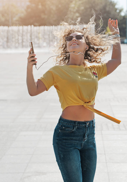 Frau mit lockigem Haar tanzt und genießt Musik im Freien mit Kopfhörern - Foto, Bild