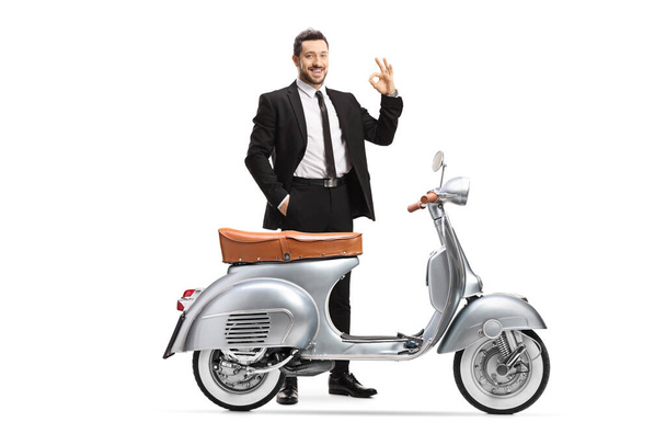 Businessman posing with a vintage silver scooter and gesturing an ok sign isolated on white background - Photo, image