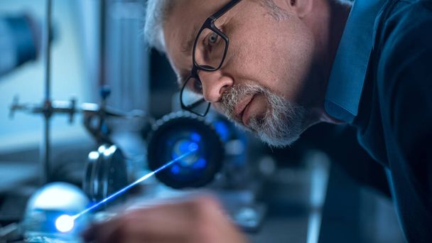 Close-up Portrait of Focused Middle Aged Engineer in Glasses Working with High Precision Laser Equipment, Using Lenses and Testing Optics for Accuracy Required Electronics - Foto, afbeelding