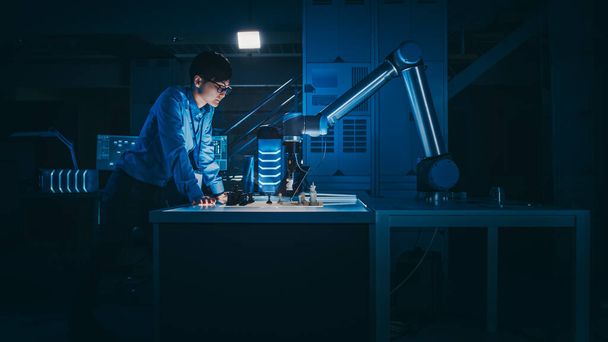 Ο Ιάπωνας μηχανικός ανάπτυξης δοκιμάζει μια διεπαφή τεχνητής νοημοσύνης παίζοντας σκάκι με ένα φουτουριστικό ρομποτικό χέρι. Βρίσκονται σε ένα Εργαστήριο Σύγχρονης Έρευνας Υψηλής Τεχνολογίας με Χαμηλό Φως Κλειδιού. - Φωτογραφία, εικόνα