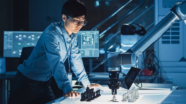 Professional Japanese Development Engineer is Testing an Artificial Intelligence Interface by Playing Chess with a Futuristic Robotic Arm. They are in a High Tech Modern Research Laboratory. - Photo, image