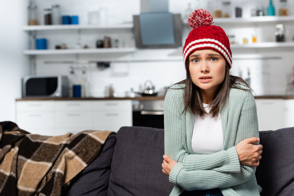 congelamento donna in maglia cappello abbracciandosi mentre seduto in cucina fredda - Foto, immagini