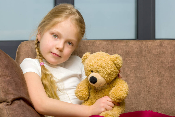 Little girl on sofa hugging teddy bear. - Fotoğraf, Görsel