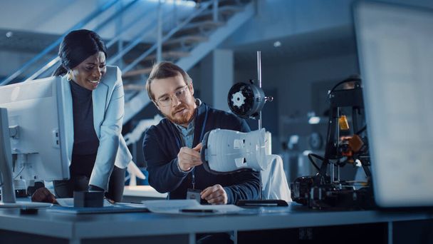 Electronics Development Engineer Working at His Desk, Talks with Project Manager, Shows Mechanism Prototype Construction. Team of Professionals Working in the Modern Technology Designing Agency.  - 写真・画像