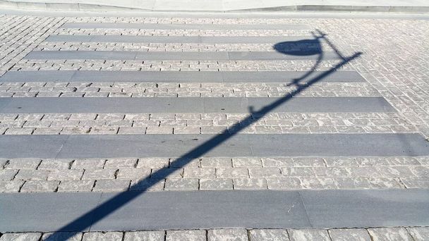 Pedestrian crosswalk made of stones. Shadow of a pole lighting the street. Paved path. Cross the road for safety reasons when people cross the street on foot. - Photo, Image