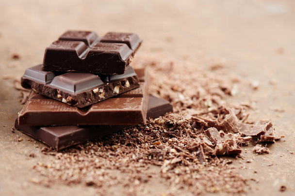 Composition of bars and pieces of different milk and dark chocolate, grated cocoa on a brown background side view close up - Photo, image