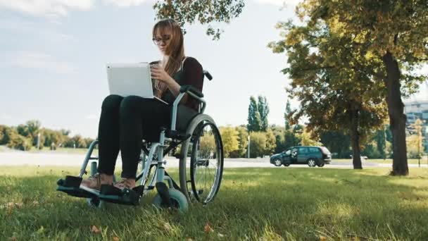Remote work concept. Young disabled woman in the wheelchair using smartphone and laptop - Footage, Video