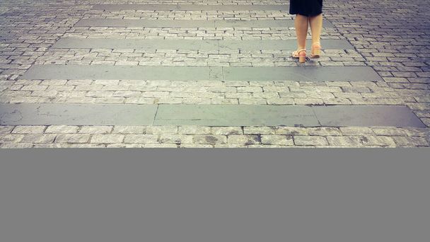 Нога девушки пересекает пешеходный переход из камней. Мощеная дорожка. Перейти дорогу в целях безопасности, когда люди переходят улицу пешком. - Фото, изображение