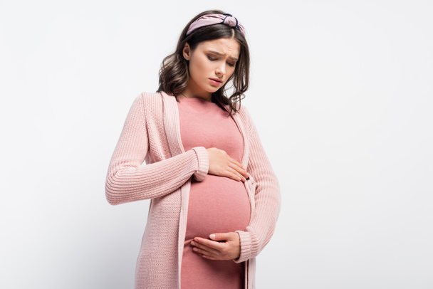 worried pregnant woman in headband touching and looking at belly on white - Fotografie, Obrázek