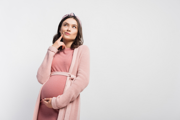 donna incinta pensierosa in fascia toccare il viso e guardando in alto isolato su bianco - Foto, immagini