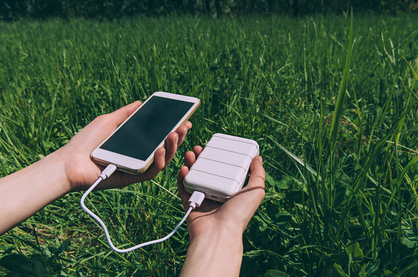 Power Bank and smartphone in the girl's hand. against the backdrop of nature - 写真・画像