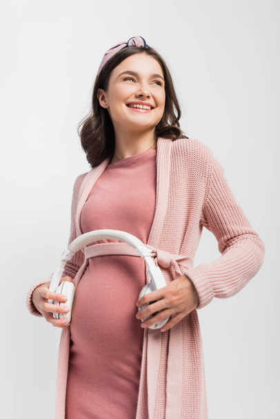 pregnant woman holding wireless headphones near belly isolated on white - 写真・画像