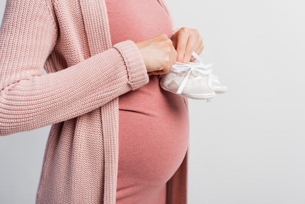 částečný pohled těhotné ženy držící dětské boty izolované na bílém - Fotografie, Obrázek