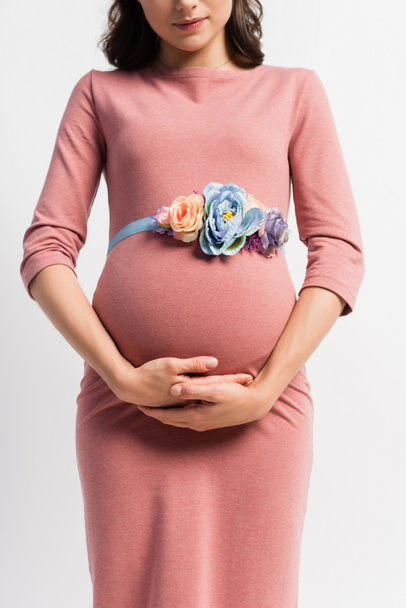vista parcial de la mujer embarazada con cinturón floral tocando barriga aislada en blanco  - Foto, Imagen