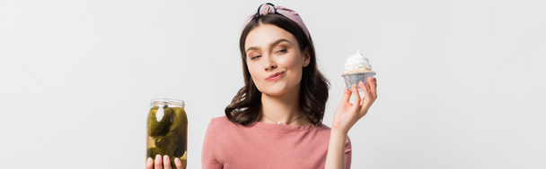 Panoramaaufnahme einer Frau, die sich zwischen Cupcake und Glas mit eingelegten Gurken auf weißem Papier entscheidet - Foto, Bild