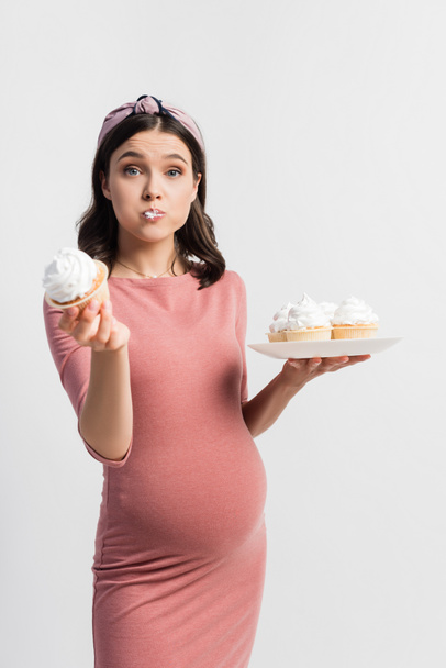 pregnant woman holding plate while eating cupcake isolated on white - Photo, image
