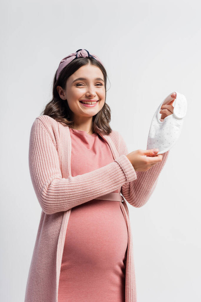 joyful pregnant woman holding small baby bib isolated on white - Fotó, kép