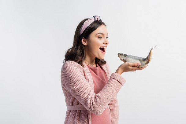 excited pregnant woman with open mouth holding dried fish isolated on white - Foto, Imagem