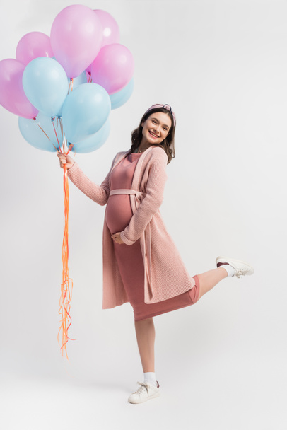 joyful and pregnant woman in dress and cardigan holding balloons on white - Photo, Image