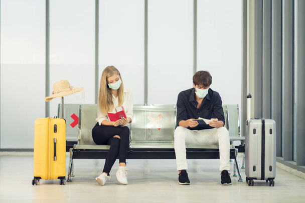 Leben während der Covid-19-Pandemie. Junger Mann und Frau warten mit Reisepass am Flughafen am Fenster auf ihren Flug  - Foto, Bild