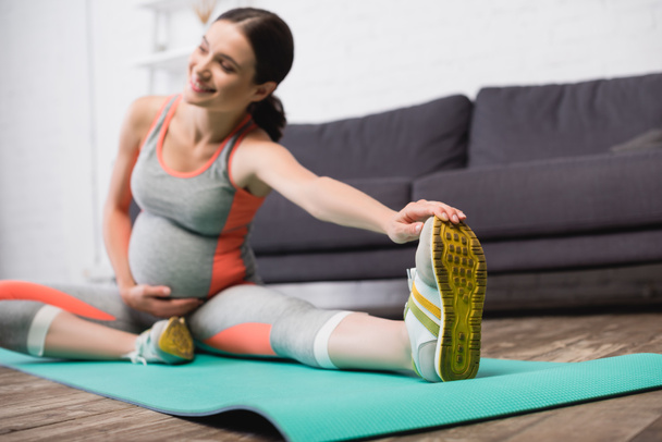 selective focus of pleased pregnant woman in sportswear stretching on fitness mat - Foto, afbeelding