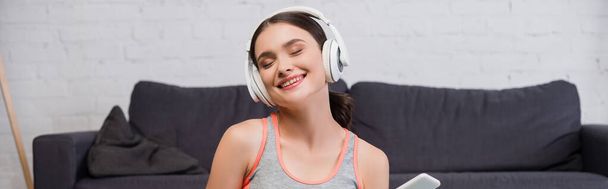 panoramic crop of pleased woman in wireless headphones listening music  - Photo, Image