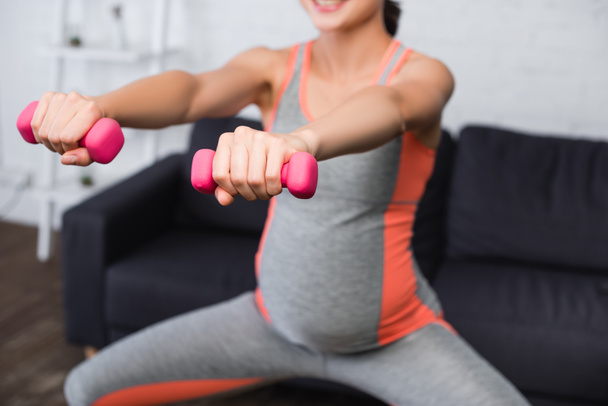 enfoque selectivo de la mujer embarazada haciendo ejercicio con pesas de color rosa en casa - Foto, imagen