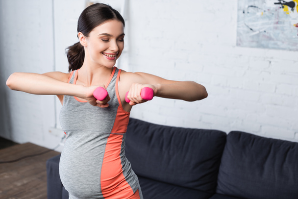 mujer embarazada feliz levantamiento de pesas pesas mancuernas de color rosa en casa - Foto, imagen