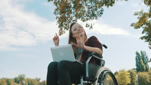Щаслива біла жінка в інвалідному візку слухає музику на ноутбуці під деревом. Низький кут
 - Кадри, відео