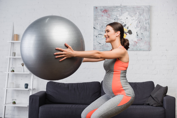 těhotná žena dělá dřep s fitness míč v obývacím pokoji  - Fotografie, Obrázek
