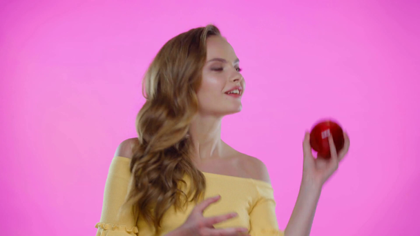 Παιχνιδιάρα νεαρή γυναίκα ρίχνει κόκκινο μήλο απομονωμένο στο ροζ - Πλάνα, βίντεο