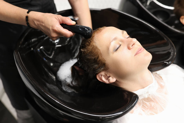 美容師はシンクでクライアントの髪から染料を洗う. - 写真・画像
