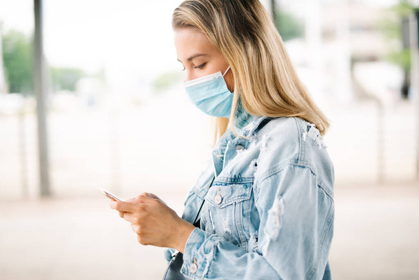 Young woman wearing antibacterial mask using phone in a city. - Zdjęcie, obraz