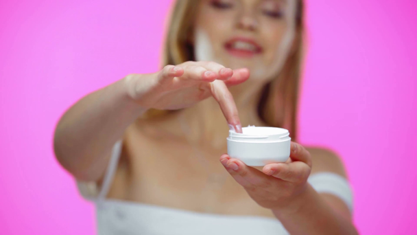 Enfoque selectivo de la mano de la mujer tocando crema cosmética aislada en rosa - Imágenes, Vídeo