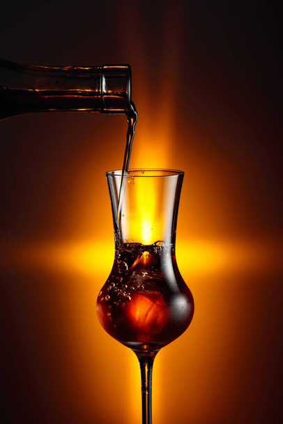 Versare la bevanda alcolica nel bicchiere con ghiaccio naturale. Bicchiere al vapore con forte bevanda alcolica.  - Foto, immagini