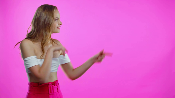 Młoda kobieta wskazująca palcami i dłońmi na biodrze odizolowana na różowo - Materiał filmowy, wideo