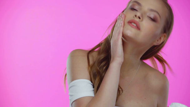 Νεαρή γυναίκα που εφαρμόζει κρέμα προσώπου ενώ ποζάρει απομονωμένη σε ροζ - Πλάνα, βίντεο