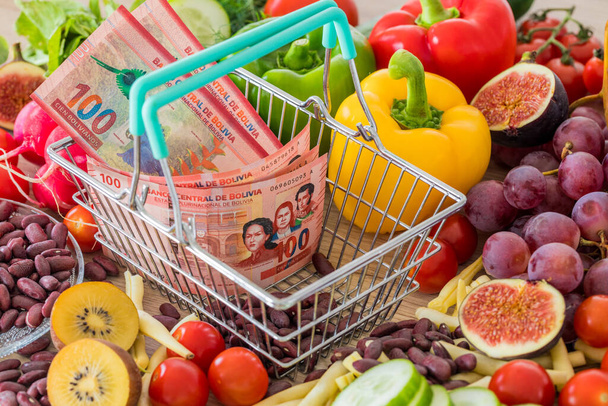 Winkelwagen met Boliviaans geld, rond voedingsmiddelen, groenten en fruit. Het concept van inflatie, stijgende prijzen en duurdere prijzen - Foto, afbeelding