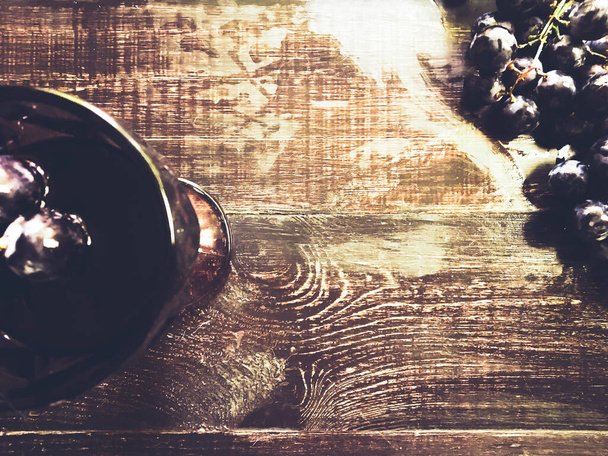 A glass with wine and grape in it on a wooden table - Foto, afbeelding