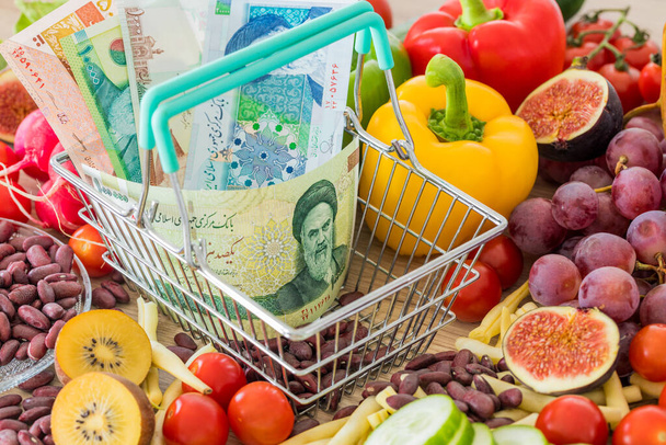 Cesta de compras con dinero iraní, alrededor de productos alimenticios, verduras y frutas. El concepto de inflación, aumento de precios y precios más caros - Foto, Imagen