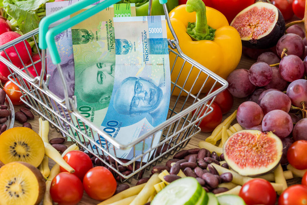Warenkorb mit indonesischem Rupia-Geld, rund um Nahrungsmittel, Gemüse und Obst. Das Konzept der Inflation, steigende Preise und teurere foo - Foto, Bild