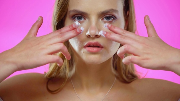 Portrait of young woman applying face cream isolated on pink - Кадри, відео