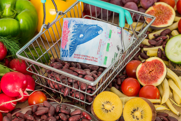 Bevásárlókosár Argentin pénzzel, élelmiszeripari termékek, zöldségek és gyümölcsök körül. Az infláció, az emelkedő árak és a drágább élelmiszerek fogalma - Fotó, kép