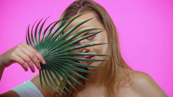 Retrato de jovem mulher tocando rosto com folha de palma isolada em rosa - Filmagem, Vídeo