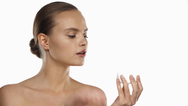 Giovane donna che tiene contenitore con crema e si applica sul viso isolato su bianco - Filmati, video