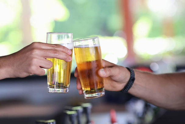 Dwie męskie ręce trzymają szklankę zimnego piwa i kieliszki. - Zdjęcie, obraz