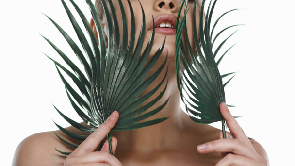 Young woman touching face with palm leaves isolated on white - Footage, Video
