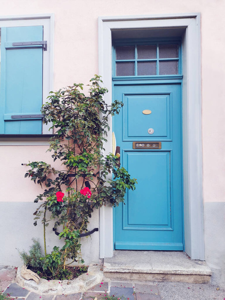 Vooraanzicht op de gevel van een Europees woongebouw met een blauwe houten deur, luiken en rode rozen op een zomerdag in de oude stad van Duitsland. Rustieke sfeer.Straatontwerp. - Foto, afbeelding